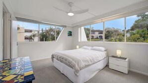 A bedroom with a bed, nightstands, a ceiling fan, and large windows. - Wickham Point - Kings Beach With Ocean Views (Kings Beach)
