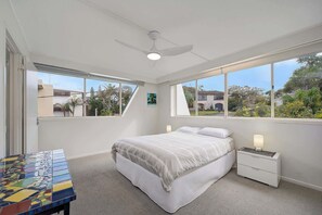 A bedroom with a bed, nightstands, a ceiling fan, and large windows.