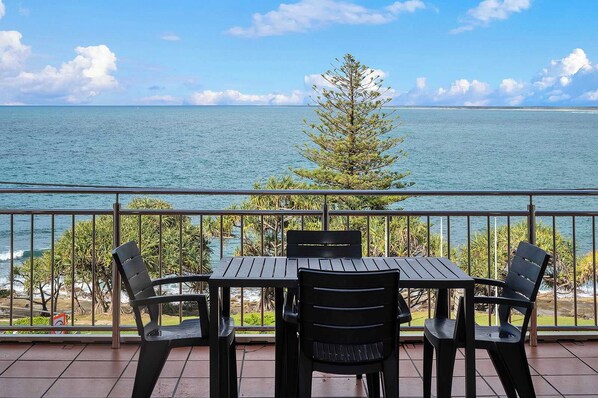 A balcony with a table and chairs overlooking a body of water and a tree.