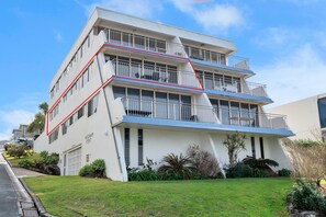 A multi-story building with a flat roof, balconies, and a well-maintained lawn.