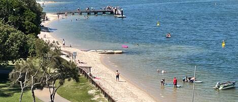 A beach with a wooden pier, clear water, and a city skyline in the background.