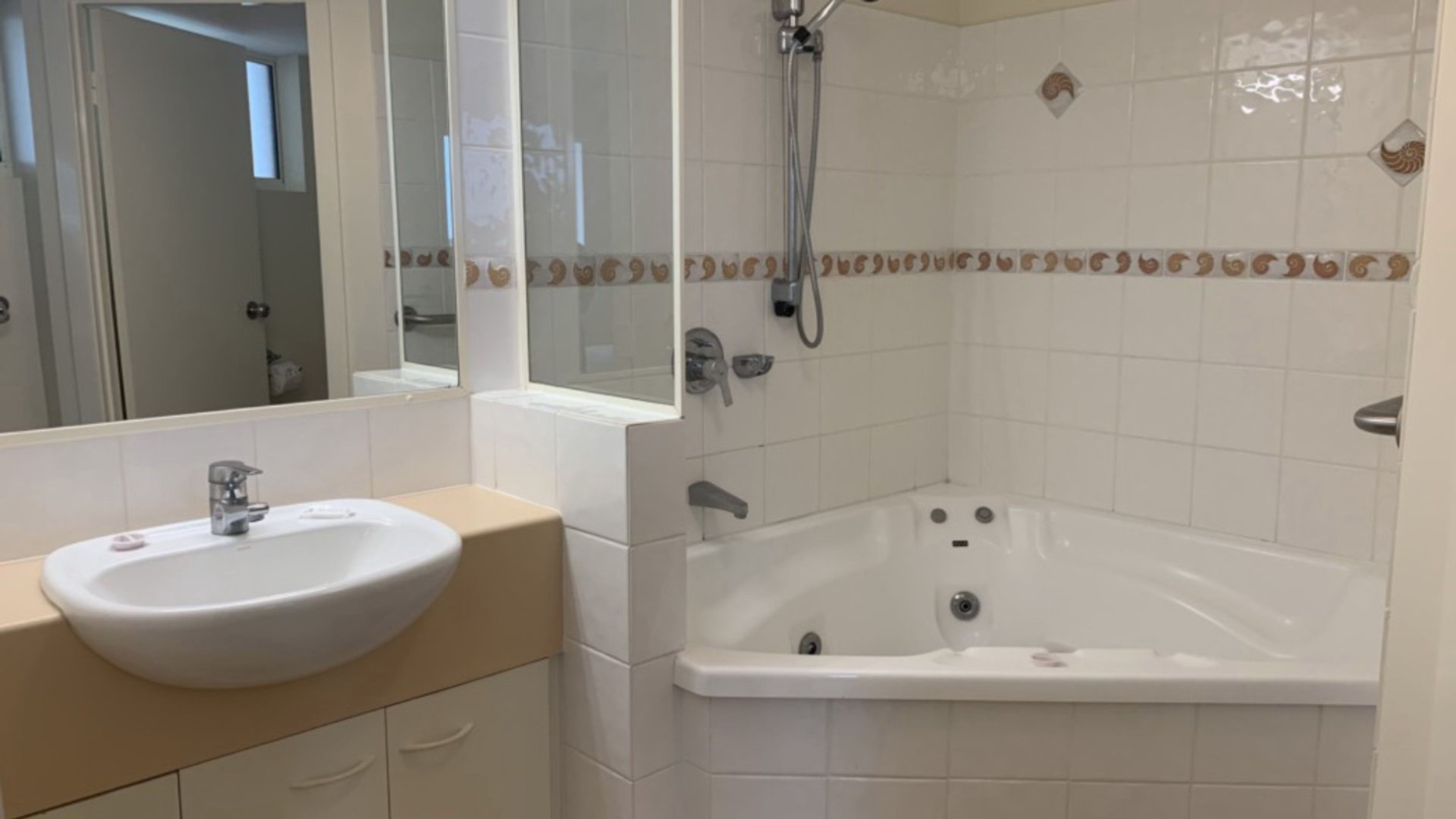 A bathroom with a white sink, vanity, and a bathtub with a showerhead.