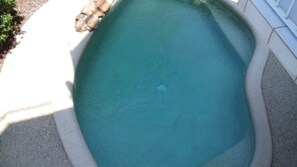 Une piscine à l’eau d’un bleu cristallin, bordée d’une margelle en béton et d’une terrasse carrelée de blanc.