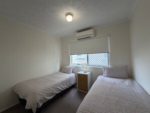 A small, clean room with two single beds, a nightstand, a lamp, and a window with blinds. - Solaris Court U2 Relax Swim and Unwind (Kings Beach)