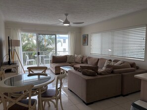 A living room with a sofa, a dining table with chairs, a ceiling fan, and a window with blinds.