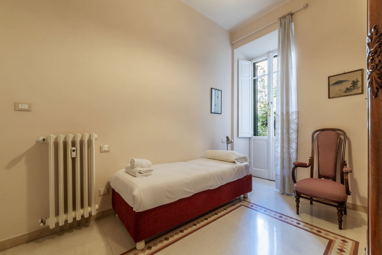 Ein Schlafzimmer mit einem Bett, einem Heizkörper, einem Sessel und einer Tür, die auf einen Balkon führt.