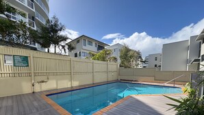 A rectangular swimming pool with a wooden deck surrounding it, a white fence, and a sign with guidelines.