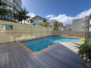 A rectangular swimming pool with a wooden deck surrounding it, a white fence, and a sign with guidelines.