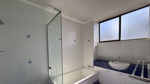 A modern bathroom with a glass shower enclosure, a freestanding bathtub, a vanity with a sink, and a window providing natural light.
