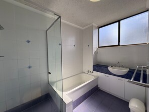 A modern bathroom with a glass shower enclosure, a freestanding bathtub, a vanity with a sink, and a window providing natural light.