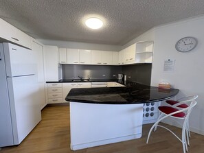 A compact kitchen with white cabinets, a black countertop island, and a clock on the wall.