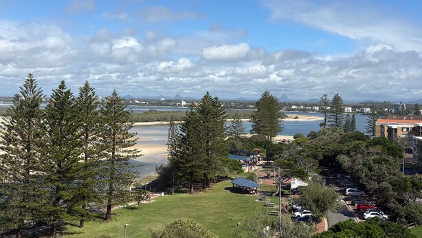 A coastal landscape with a beach, trees, and a parking area.