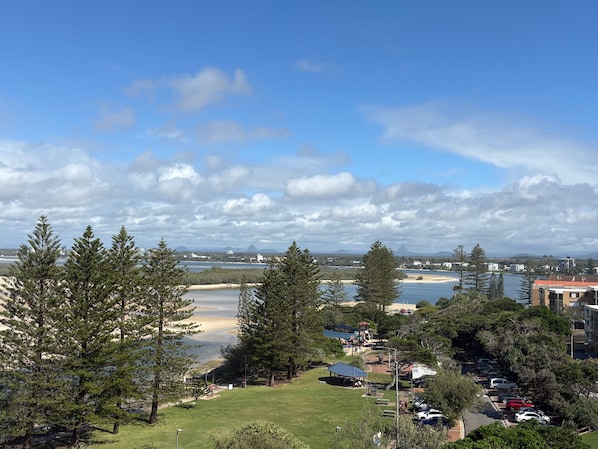 A coastal landscape with a beach, trees, and a parking area.