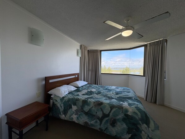 A bedroom with a bed, a nightstand, a ceiling fan, and a window with curtains.