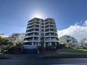 A multi-story residential building with a garage entrance, surrounded by greenery and other buildings.