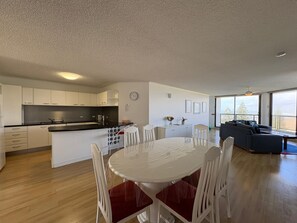 A modern kitchen with white cabinets, a black countertop, and a dining area with a white table and red chairs.