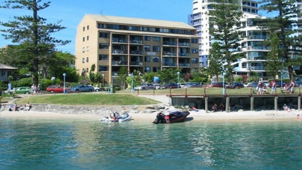 A waterfront property with a building featuring multiple balconies, a sandy beach, and a dock area. - Allamanda Place U5 Bulcock Beach Waterfront Views (Caloundra)