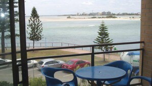 A balcony with a view of the sea, a parking area with cars, and a building in the distance. - Allamanda Place U5 Bulcock Beach Waterfront Views (Caloundra)