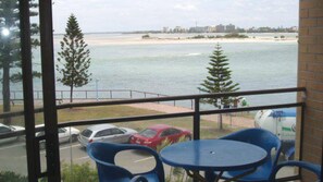 A balcony with a view of the sea, a parking area with cars, and a building in the distance. - Allamanda Place U5 Bulcock Beach Waterfront Views (Caloundra)