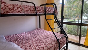 Ein Stockbett mit gemusterten Betttextilien, ein Fenster mit Blick ins Freie und ein gelber Vorhang.