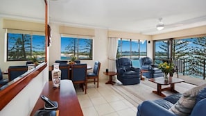 A spacious living area with a balcony, large windows, and a view of the beach. - Lowanna U8 | Absolute Waterfront at Bulcock Beach (Golden Beach)