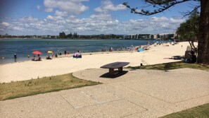 Una playa con mesa de picnic, sombrillas y gente.