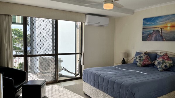Habitación de hotel con cama, escritorio, silla, un cuadro y vistas a través de un ventanal.
