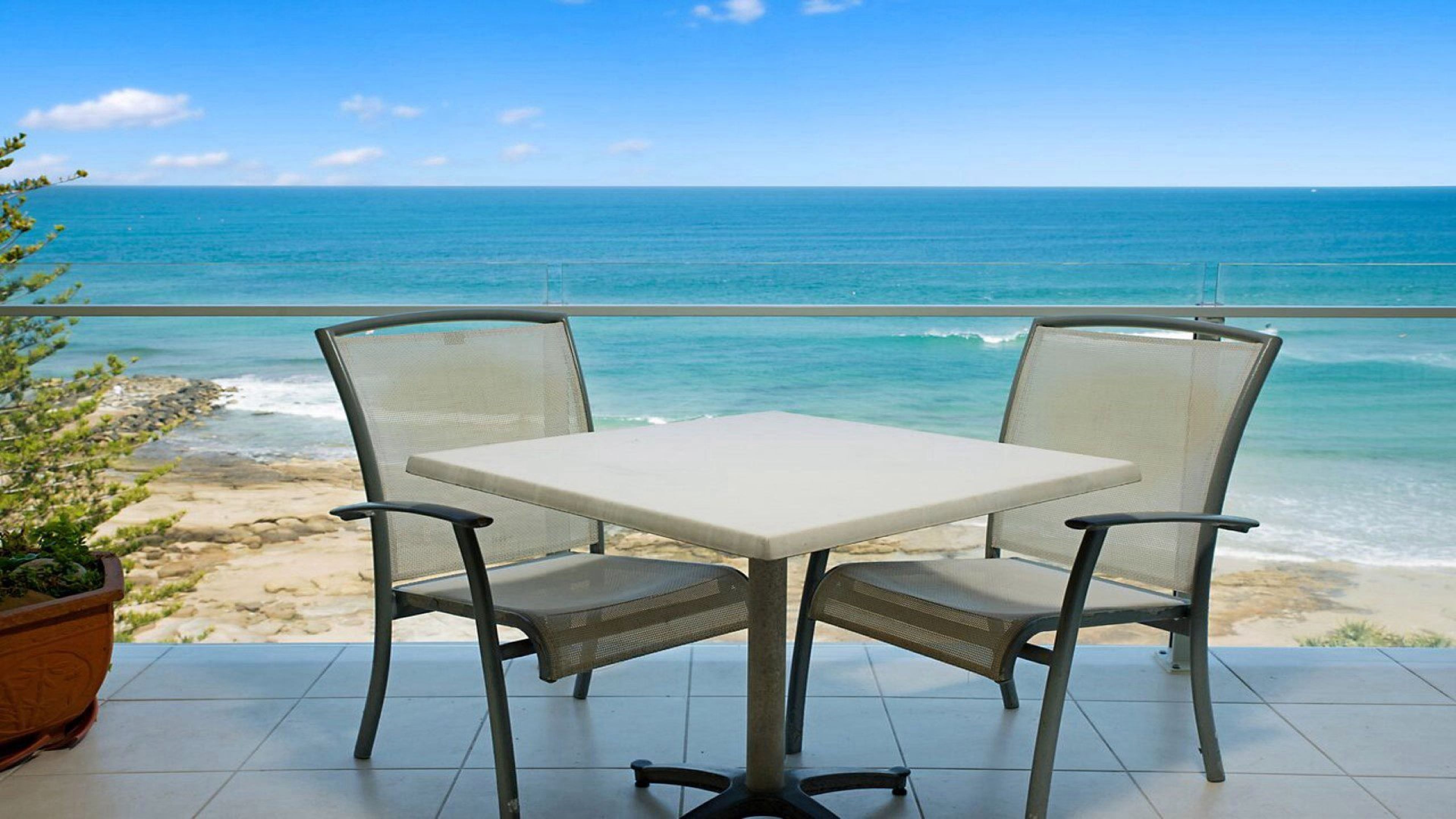 Un balcón con mesa y dos sillas con vista a la playa y el océano.