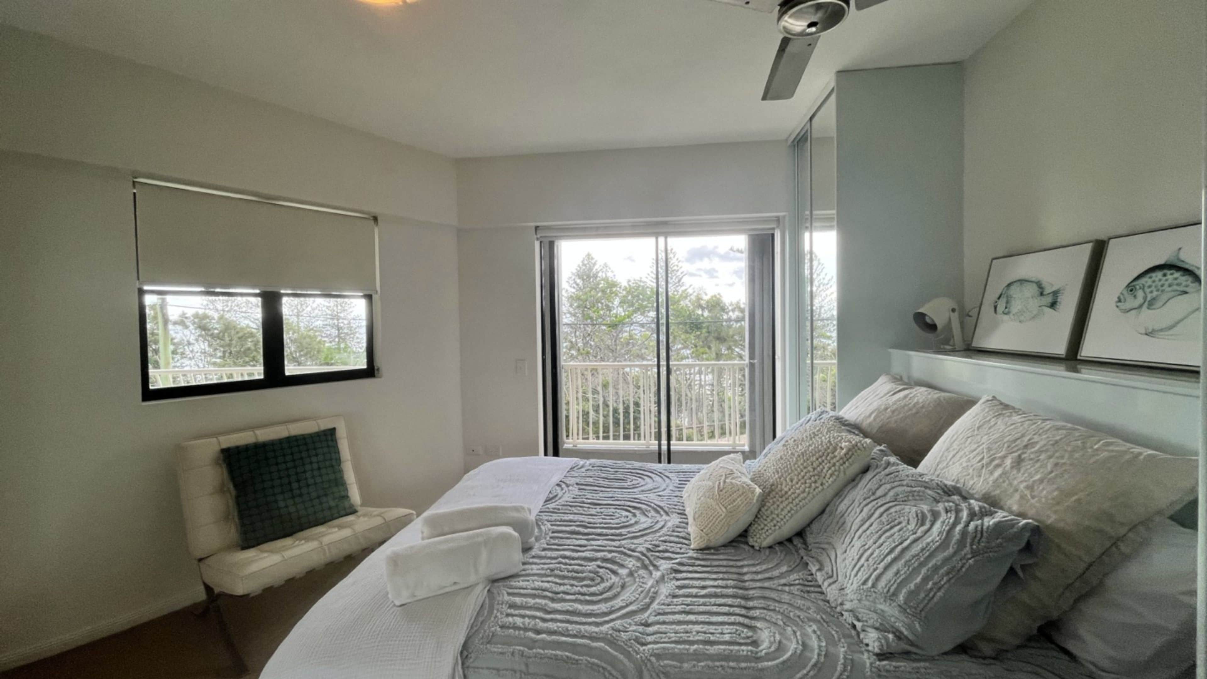 Een slaapkamer met een bed, een raam en een balkon.