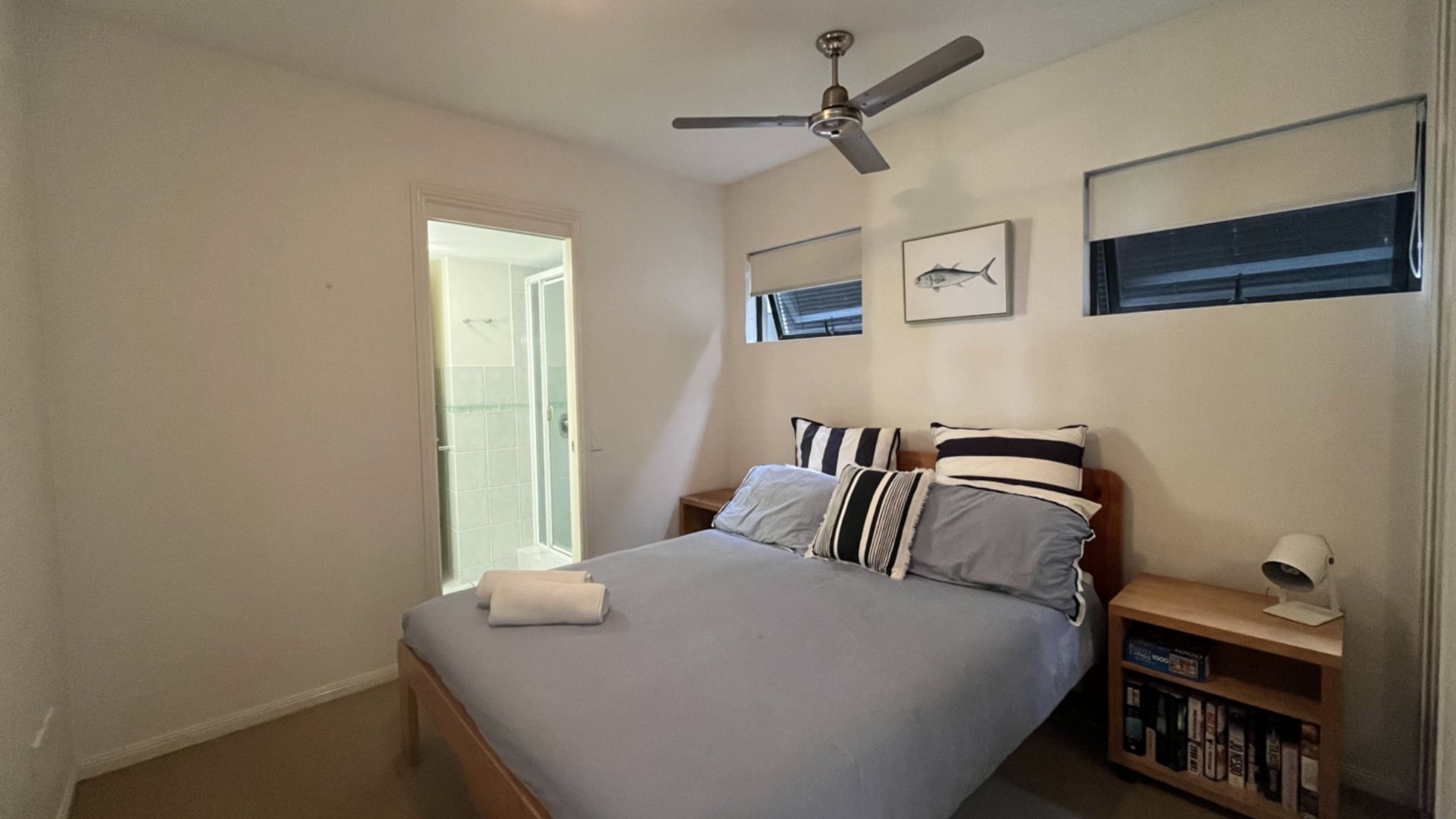 A bedroom with a bed, a ceiling fan, a nightstand, and a bookshelf.