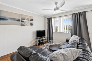 A modern living room with a leather sofa, a glass coffee table, a flat-screen TV, and a ceiling fan. - Beachside Court U9, Kings Beach Escape (Kings Beach)