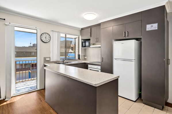 A modern kitchen with a central island, stainless steel appliances, and a view to the outside. - Beachside Court U9, Kings Beach Escape (Kings Beach)