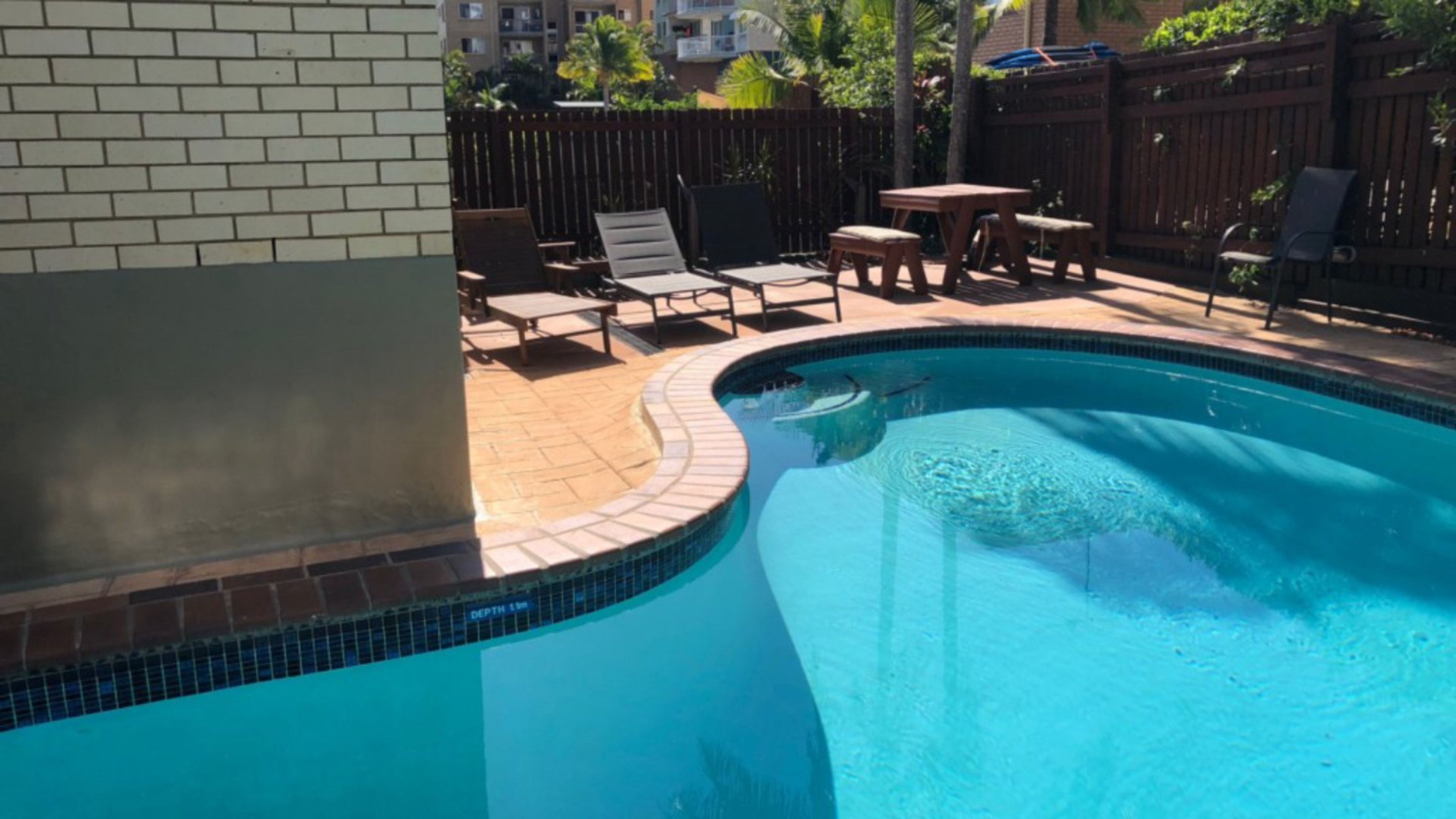 A swimming pool with a tiled edge, surrounded by a wooden fence, and outdoor furniture.