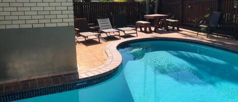 A swimming pool with a tiled edge, surrounded by a wooden fence, and outdoor furniture.
