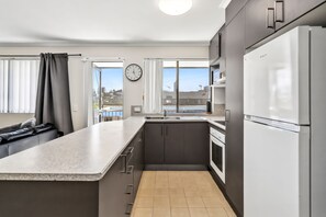 A modern kitchen with a large island, built-in appliances, and a view of the city. - Beachside Court U9, Kings Beach Escape (Kings Beach)