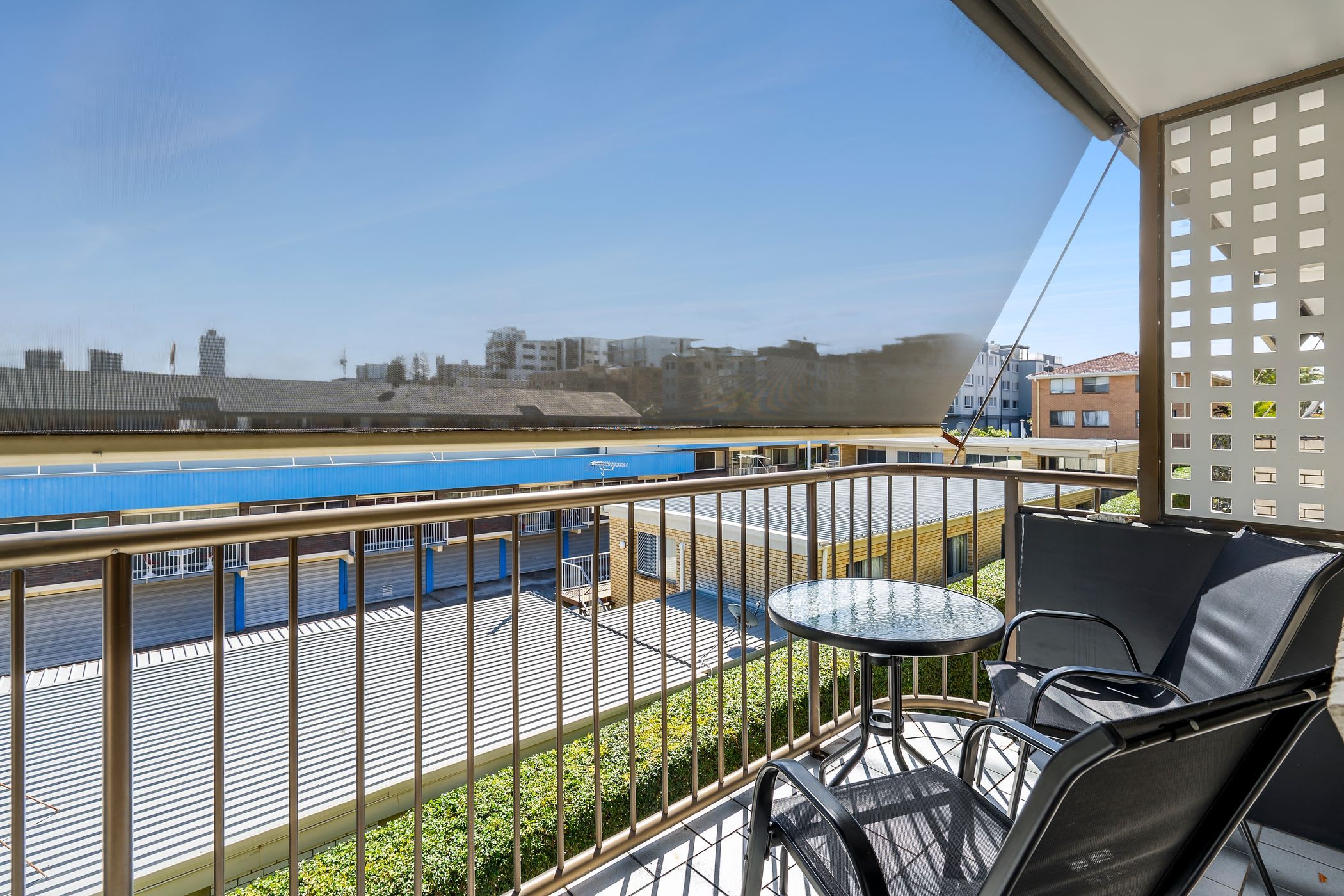 Ein Balkon mit Tisch und Stühlen, mit Blick auf einen Fluss, im Hintergrund ein blaues Gebäude.