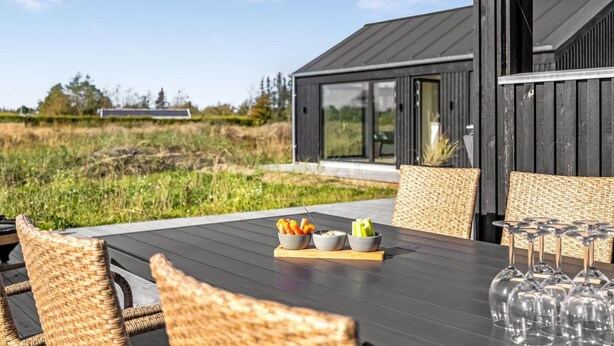 An outdoor dining area with wicker chairs, a table with a bowl of snacks, and wine glasses.