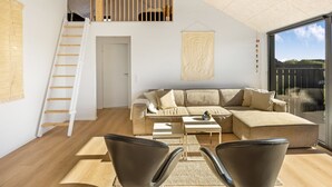 A modern living room with a large sectional sofa, a coffee table, and two leather chairs. A wooden staircase leads to an upper level.
