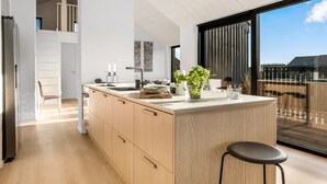 A modern kitchen with a large island, wooden cabinets, and a view of the outdoors through large windows.