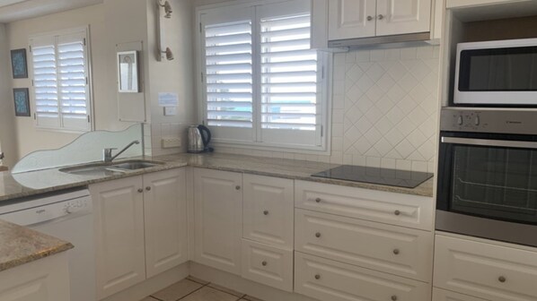 A kitchen with white cabinets, a sink, a kettle, and a microwave.