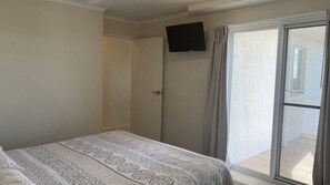A bedroom with a bed, a door, a television mounted on the wall, and a sliding glass door leading to an outdoor area.