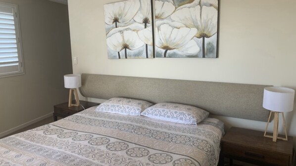 A bedroom with a bed, two bedside tables, a headboard, and a wall-mounted painting. - The Entrance Currimundi Lakefront Escape | Pool & Ocean Views (Currimundi)