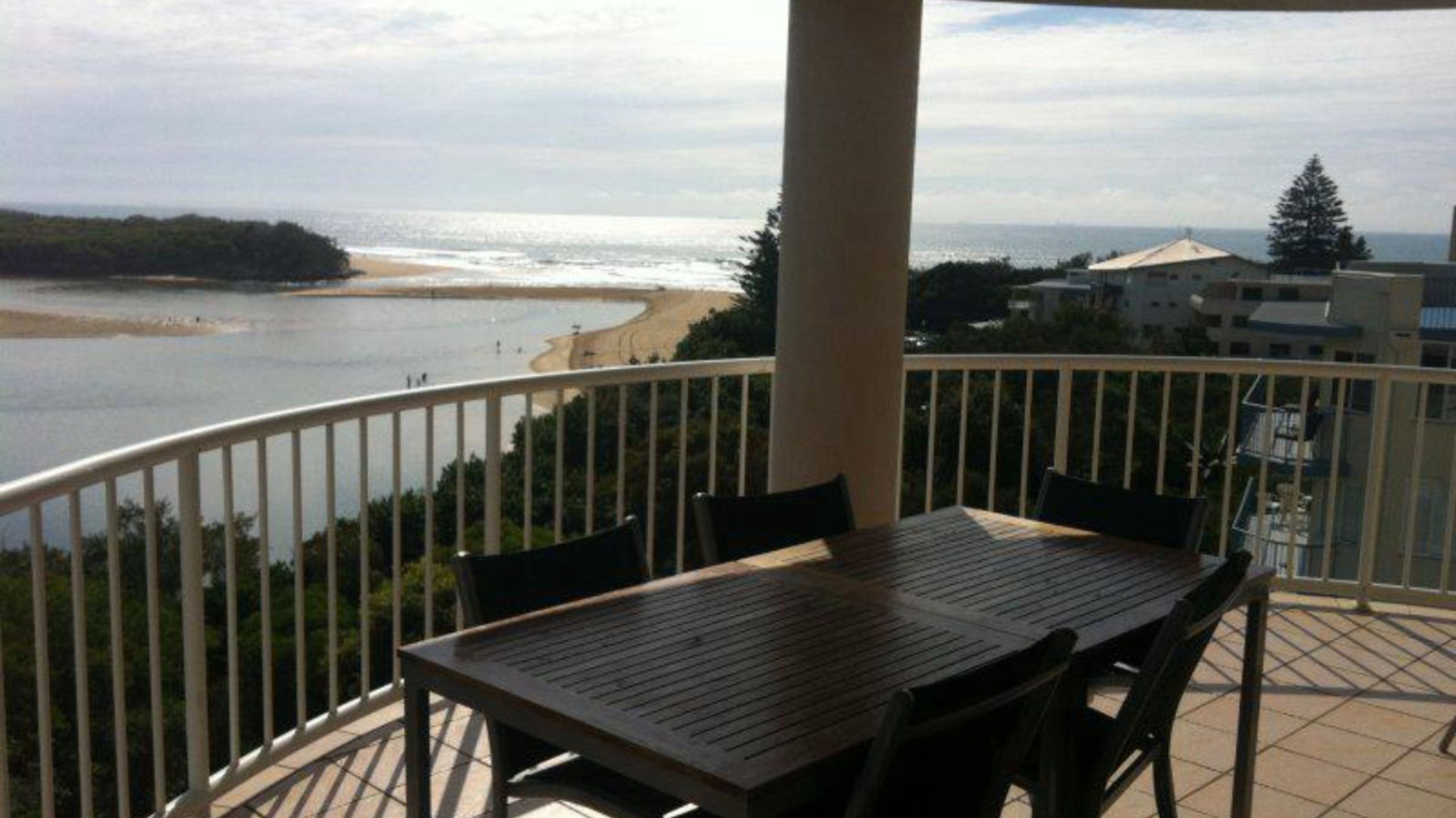 A balcony with a table and chairs, overlooking a beach and ocean.