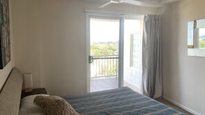 A bedroom with a bed, a nightstand, a window with a view of greenery, and a ceiling fan. - The Entrance Currimundi Lakefront Escape | Pool & Ocean Views (Currimundi)