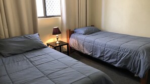 Una habitación con dos camas, una mesita de noche con lámpara y una ventana con cortinas.