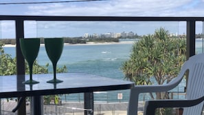 Un balcon avec vue sur la mer, une table avec deux verres verts et une chaise blanche.