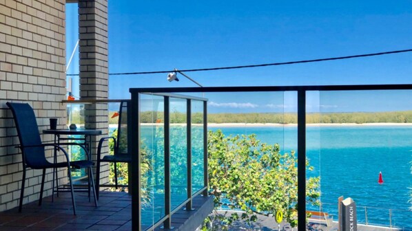 Ein Balkon mit Glasgeländer mit Blick auf einen Strand und das Wasser.