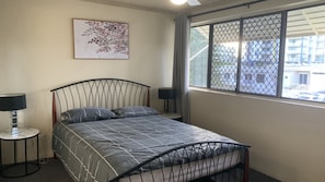Ein Schlafzimmer mit einem Bett, zwei Nachttischen, einem Fenster mit Blick und einem Wandbild.