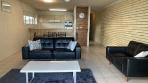 A living room with two black leather sofas, a white coffee table, and a kitchen in the background.