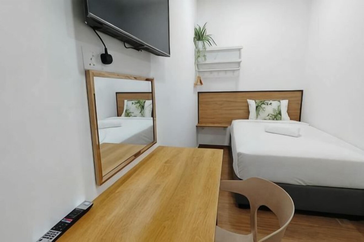 A hotel room with a bed, a TV mounted on the wall, a wooden desk, and a chair.